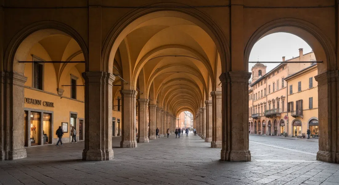 El Pórtico de San Luca se pierde en un largo túnel ocre de arcos desde Porta Saragozza, luz matutina y acera vacía