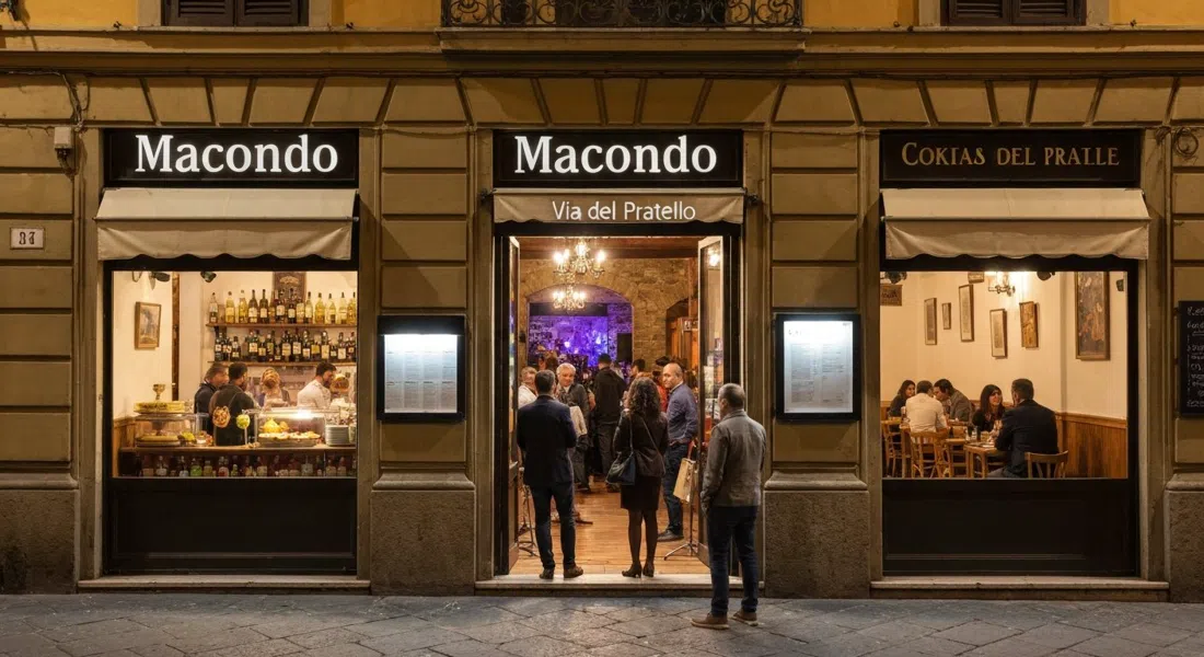 el frente de Macondo en Via del Pratello de noche, el bufé de aperitivo brillando en el interior mientras una pequeña multitud se apoya en la entrada con música en vivo saliendo de la parte trasera